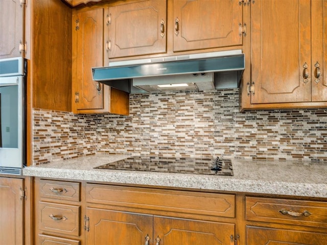 7600 NW 27th St, Bethany, OK 73008 - kitchen featuring under cabinet range hood, light countertops, backsplash, oven, and brown cabinetry