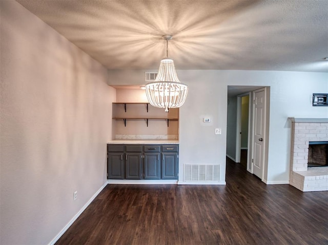 3003 River Oaks Dr Unit 119, Norman, OK 73072 - unfurnished dining area with a chandelier, dark wood finished floors, a fireplace, and a textured ceiling