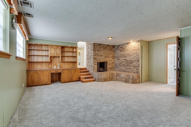 5932 N Grove Ave, Oklahoma City, OK 73122 - unfurnished living room featuring a brick fireplace, built in desk, a textured ceiling, light colored carpet, and wooden walls