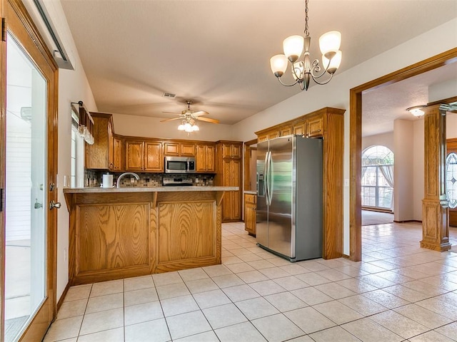 1204 Scrambler Ln, Edmond, OK 73025 - kitchen with stainless steel appliances, a peninsula, decorative backsplash, brown cabinets, and light tile patterned floors