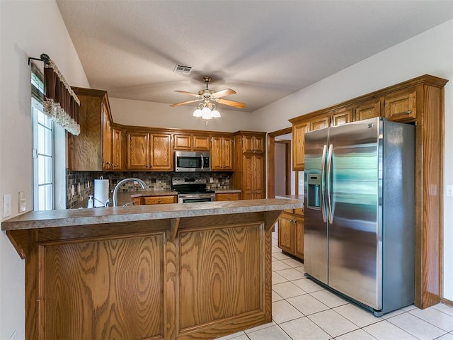 1204 Scrambler Ln, Edmond, OK 73025 - kitchen featuring stainless steel appliances, a peninsula, backsplash, brown cabinetry, and light tile patterned floors