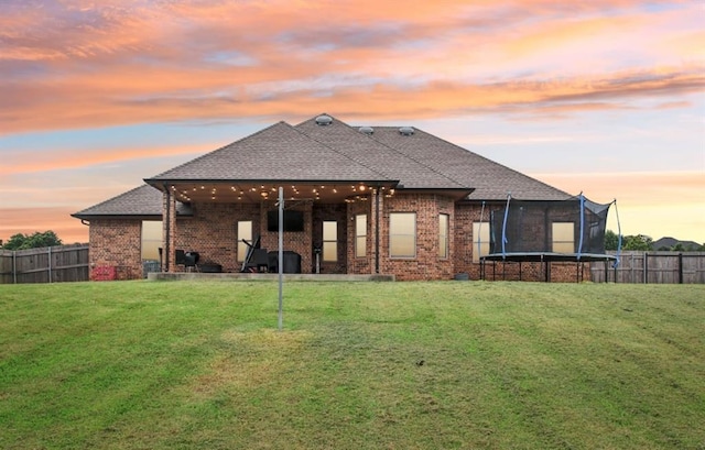 7732 Jesse Trl, Oklahoma City, OK 73150 - back of house at dusk featuring a trampoline, brick siding, a fenced backyard, and a shingled roof