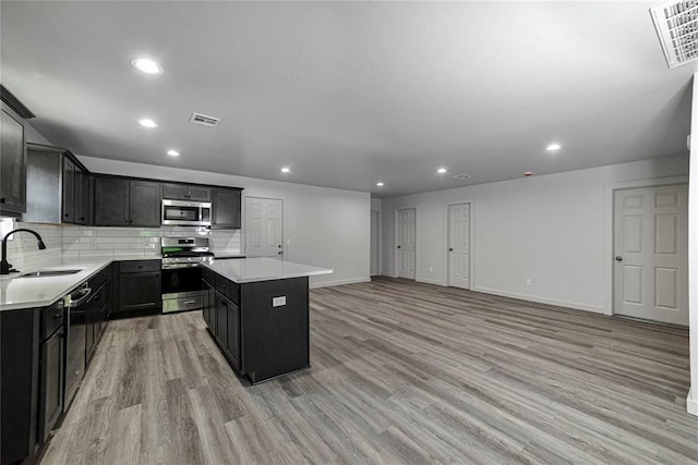 1417 Mallard Dr, Del City, OK 73115 - kitchen with appliances with stainless steel finishes, a center island, light wood-style flooring, dark cabinetry, and recessed lighting