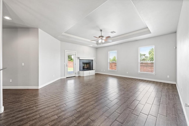 641 Geneva Dr, Edmond, OK 73025 - unfurnished living room featuring a raised ceiling, dark wood-type flooring, a ceiling fan, and a tiled fireplace