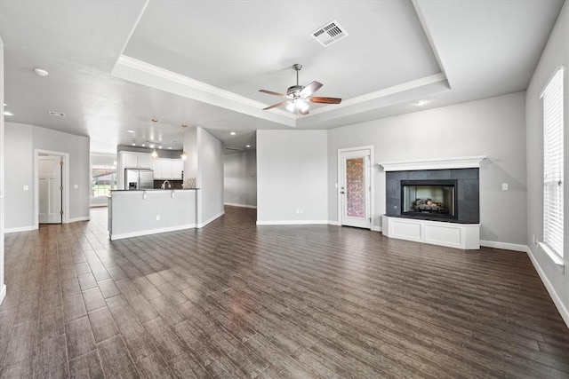 641 Geneva Dr, Edmond, OK 73025 - unfurnished living room featuring a raised ceiling, ceiling fan, a fireplace, and dark wood-type flooring