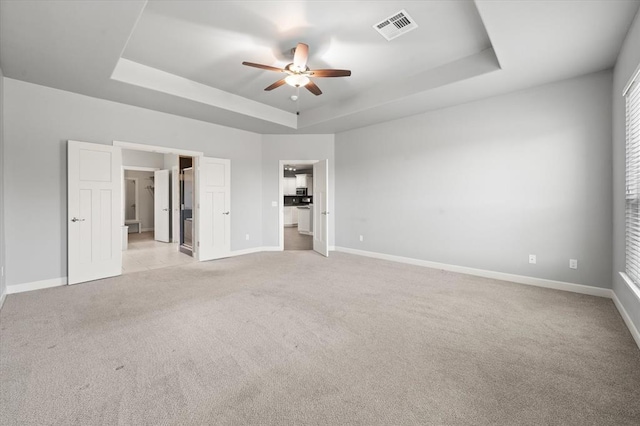 641 Geneva Dr, Edmond, OK 73025 - unfurnished bedroom featuring a tray ceiling, light carpet, a walk in closet, and a ceiling fan