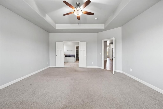 641 Geneva Dr, Edmond, OK 73025 - unfurnished bedroom with a tray ceiling, light colored carpet, ensuite bathroom, and a ceiling fan
