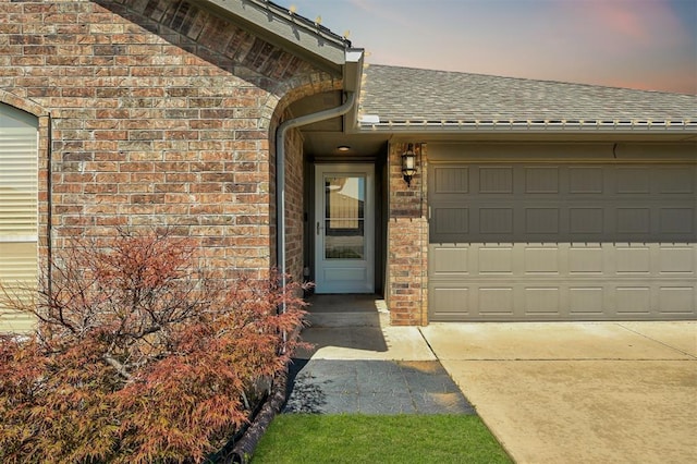 1109 Hickory Creek Dr, Yukon, OK 73099 - exterior entry at dusk featuring a shingled roof, brick siding, driveway, and a garage