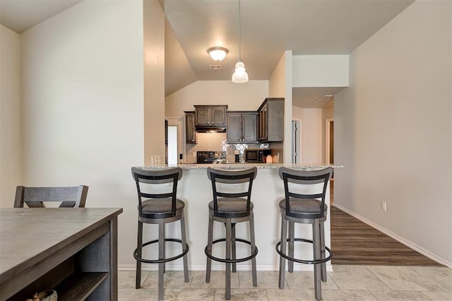 1109 Hickory Creek Dr, Yukon, OK 73099 - kitchen with dark brown cabinets, a breakfast bar, electric range oven, under cabinet range hood, and tasteful backsplash