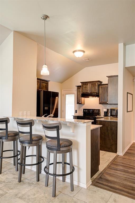 1109 Hickory Creek Dr, Yukon, OK 73099 - kitchen with black appliances, dark brown cabinets, under cabinet range hood, a breakfast bar, and a peninsula