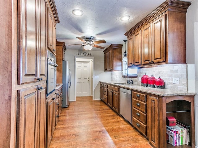 2349 Fox Ln, Blanchard, OK 73010 - kitchen featuring appliances with stainless steel finishes, brown cabinetry, backsplash, ceiling fan, and light wood-type flooring