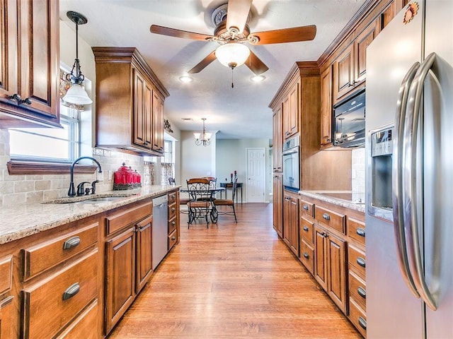 2349 Fox Ln, Blanchard, OK 73010 - kitchen with stainless steel appliances, brown cabinetry, tasteful backsplash, light wood-type flooring, and decorative light fixtures