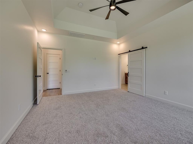 7625 Leoma Ln, Oklahoma City, OK 73150 - unfurnished bedroom with light carpet, a barn door, a tray ceiling, and a ceiling fan