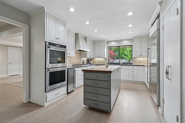 11209 Thorn Ridge Rd, Oklahoma City, OK 73120 - kitchen featuring appliances with stainless steel finishes, premium range hood, wood counters, light wood-type flooring, and recessed lighting