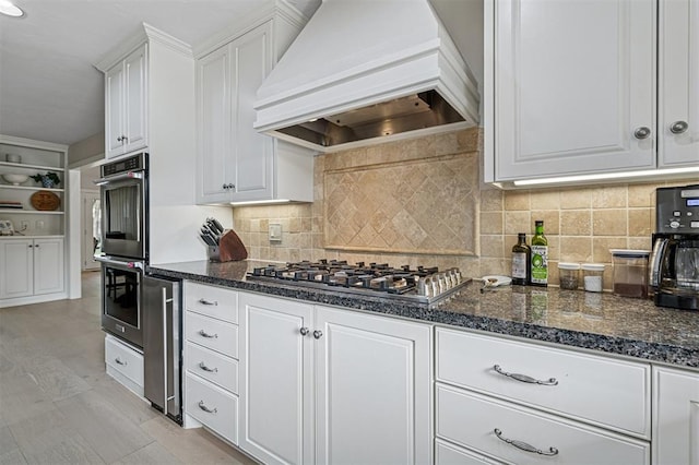11209 Thorn Ridge Rd, Oklahoma City, OK 73120 - kitchen featuring custom range hood, appliances with stainless steel finishes, white cabinets, dark stone countertops, and tasteful backsplash