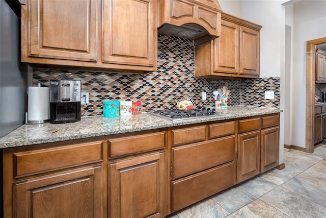 6813 Chelsey Ln, Oklahoma City, OK 73132 - kitchen with backsplash, stainless steel gas stovetop, brown cabinets, light stone counters, and light stone finish floors