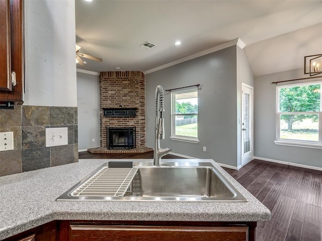 3922 Deer Xing, Edmond, OK 73025 - kitchen with healthy amount of natural light, a ceiling fan, a brick fireplace, dark wood-style flooring, and ornamental molding