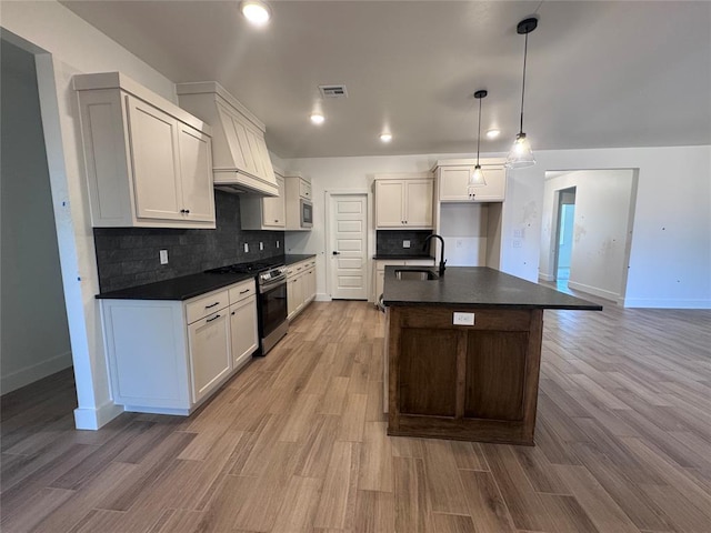 6101 Kinnick Dr, Edmond, OK 73034 - kitchen with dark countertops, stainless steel appliances, backsplash, light wood-style floors, and a kitchen island with sink