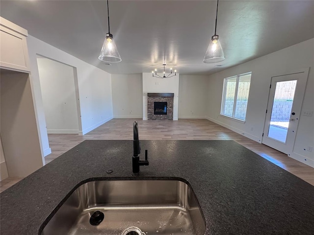 6101 Kinnick Dr, Edmond, OK 73034 - kitchen with wood finished floors, a fireplace, pendant lighting, dark stone counters, and a chandelier