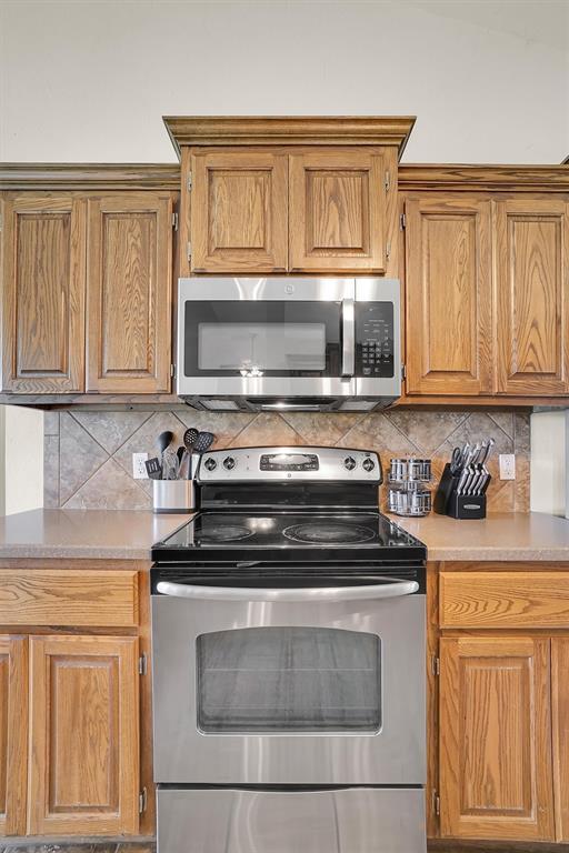 1809 Foxtail Cir, Altus, OK 73521 - kitchen featuring appliances with stainless steel finishes, tasteful backsplash, light countertops, and brown cabinetry