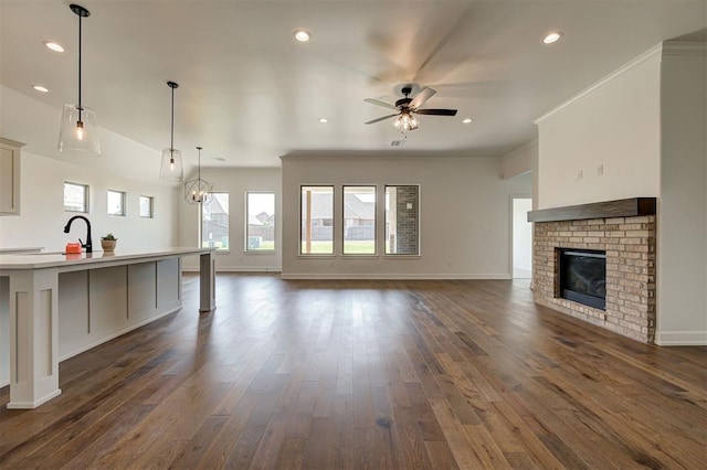 3328 Slate River Dr, Yukon, OK 73099 - unfurnished living room featuring a ceiling fan, dark wood finished floors, a brick fireplace, recessed lighting, and crown molding