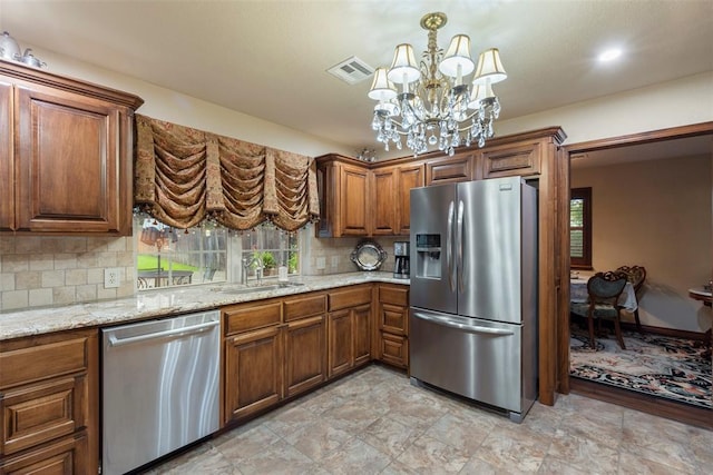 2 Terra Ln, Shawnee, OK 74804 - kitchen with stainless steel appliances, a chandelier, brown cabinetry, tasteful backsplash, and light stone counters
