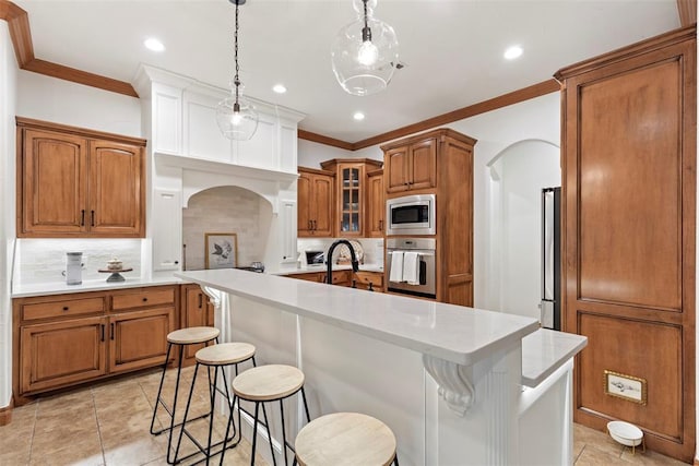 1900 Cobblestone Dr, Shawnee, OK 74804 - kitchen featuring appliances with stainless steel finishes, ornamental molding, arched walkways, brown cabinetry, and a center island with sink