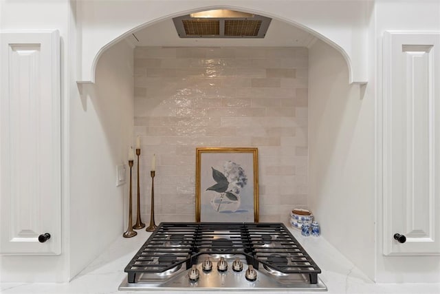 1900 Cobblestone Dr, Shawnee, OK 74804 - kitchen view of stainless steel gas cooktop, white cabinetry, arched walkways, backsplash, and light countertops