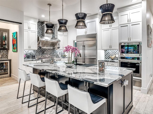 2824 Guilford Ln, Oklahoma City, OK 73120 - kitchen with appliances with stainless steel finishes, beverage cooler, wall chimney range hood, recessed lighting, and decorative backsplash
