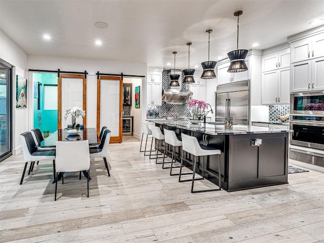 2824 Guilford Ln, Oklahoma City, OK 73120 - kitchen featuring stainless steel appliances, light wood-style floors, a warming drawer, a barn door, and decorative backsplash