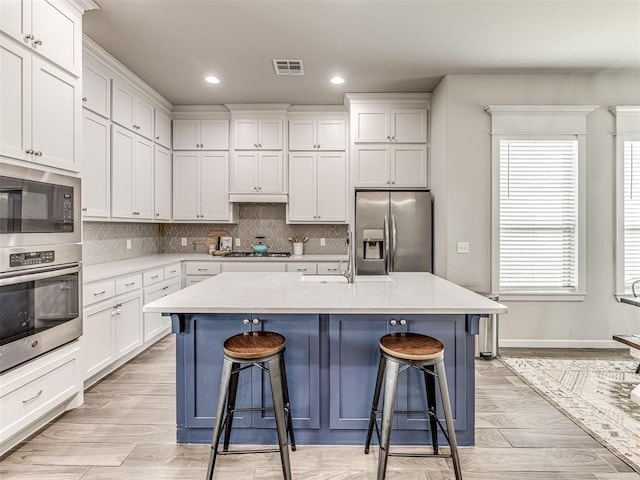 11104 Fairways Ave, Yukon, OK 73099 - kitchen with stainless steel appliances, a kitchen breakfast bar, white cabinetry, a center island with sink, and decorative backsplash
