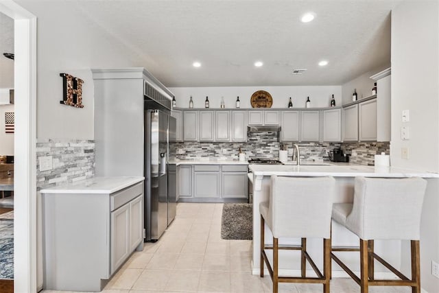 1800 NW 161st Pl, Edmond, OK 73013 - kitchen featuring gray cabinetry, a kitchen breakfast bar, backsplash, under cabinet range hood, and light countertops