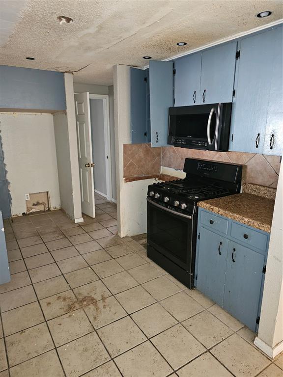 1137 Mallard Dr, Del City, OK 73115 - kitchen with black appliances, blue cabinets, light tile patterned flooring, a textured ceiling, and dark countertops