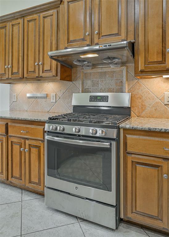 5404 NW 119th St, Oklahoma City, OK 73162 - kitchen with gas range, under cabinet range hood, brown cabinets, and light stone countertops