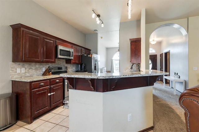 2001 Fair Meadow Dr, Edmond, OK 73003 - kitchen with appliances with stainless steel finishes, a breakfast bar area, decorative backsplash, light stone countertops, and arched walkways