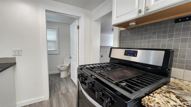 1401 W College Ave, Guthrie, OK 73044 - kitchen featuring gas range oven, white cabinetry, wood finished floors, and decorative backsplash