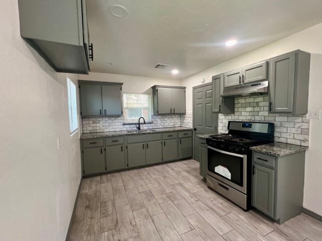 4020 NW 28th St, Oklahoma City, OK 73107 - kitchen featuring stainless steel gas stove, under cabinet range hood, light wood-type flooring, tasteful backsplash, and gray cabinetry