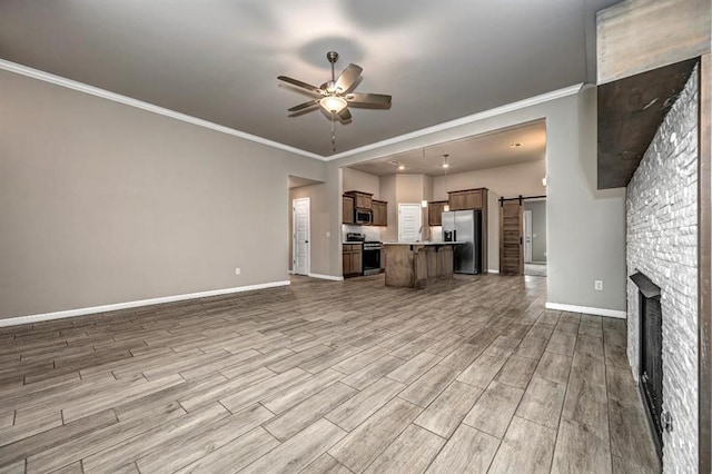 4217 NW 151st St, Edmond, OK 73013 - unfurnished living room with a ceiling fan, a barn door, wood finished floors, ornamental molding, and a stone fireplace