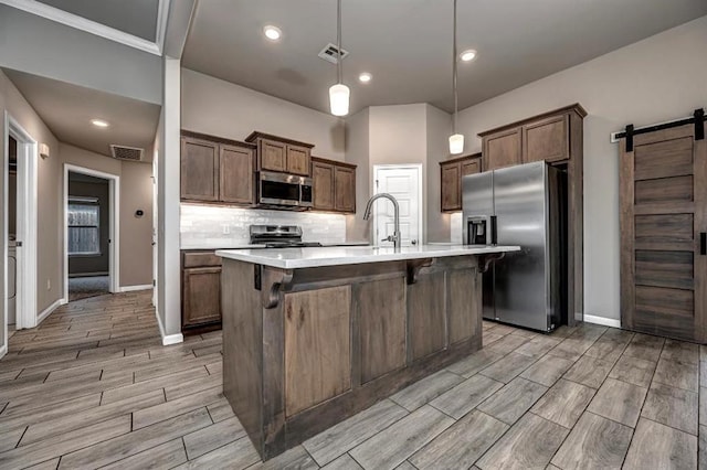 4217 NW 151st St, Edmond, OK 73013 - kitchen featuring appliances with stainless steel finishes, a barn door, wood tiled floors, light countertops, and a kitchen bar