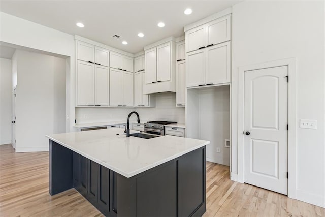 1690 Shaylee Ln, Choctaw, OK 73020 - kitchen with light wood-style floors, white cabinets, stainless steel range, light countertops, and a kitchen island with sink
