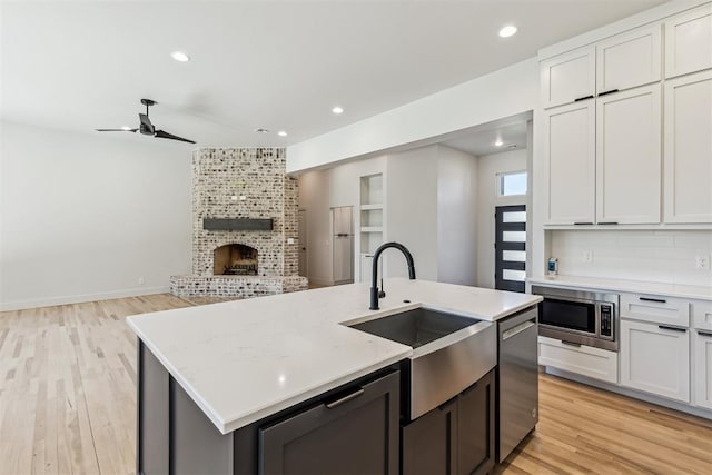 1690 Shaylee Ln, Choctaw, OK 73020 - kitchen with stainless steel appliances, a fireplace, a center island with sink, light wood finished floors, and a ceiling fan