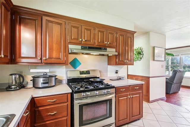 213 Country Club Ter, Oklahoma City, OK 73110 - kitchen with under cabinet range hood, stainless steel gas stove, light countertops, and light tile patterned floors