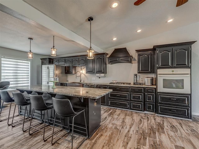 111 E Memorial, Marlow, OK 73055 - kitchen with stainless steel appliances, custom range hood, a kitchen breakfast bar, light stone counters, and a kitchen island