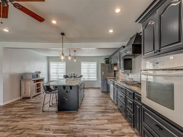 111 E Memorial, Marlow, OK 73055 - kitchen with stainless steel appliances, wall chimney exhaust hood, a center island, wood finished floors, and recessed lighting
