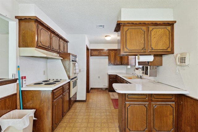 929 NE 5th St, Moore, OK 73160 - kitchen with white electric cooktop, a peninsula, light floors, under cabinet range hood, and brown cabinetry