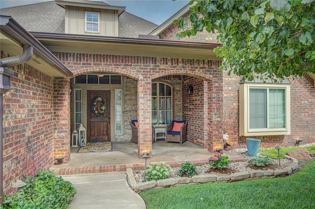 property entrance featuring brick siding, covered porch, and roof with shingles