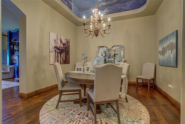 dining area featuring a raised ceiling, wood finished floors, a chandelier, and arched walkways