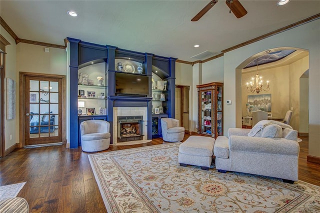 living room featuring ornamental molding, arched walkways, ceiling fan, a tiled fireplace, and a chandelier