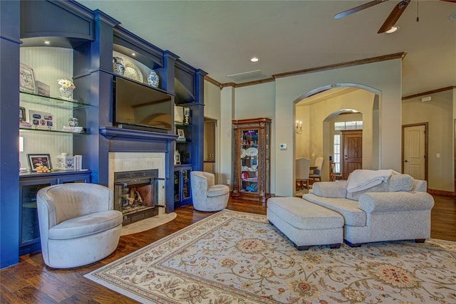 living area with ceiling fan, ornamental molding, a tile fireplace, arched walkways, and wood finished floors