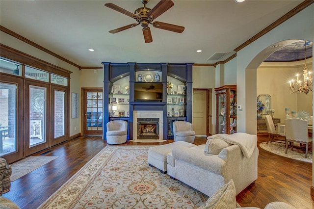 living room featuring ornamental molding, a tile fireplace, arched walkways, wood finished floors, and a chandelier
